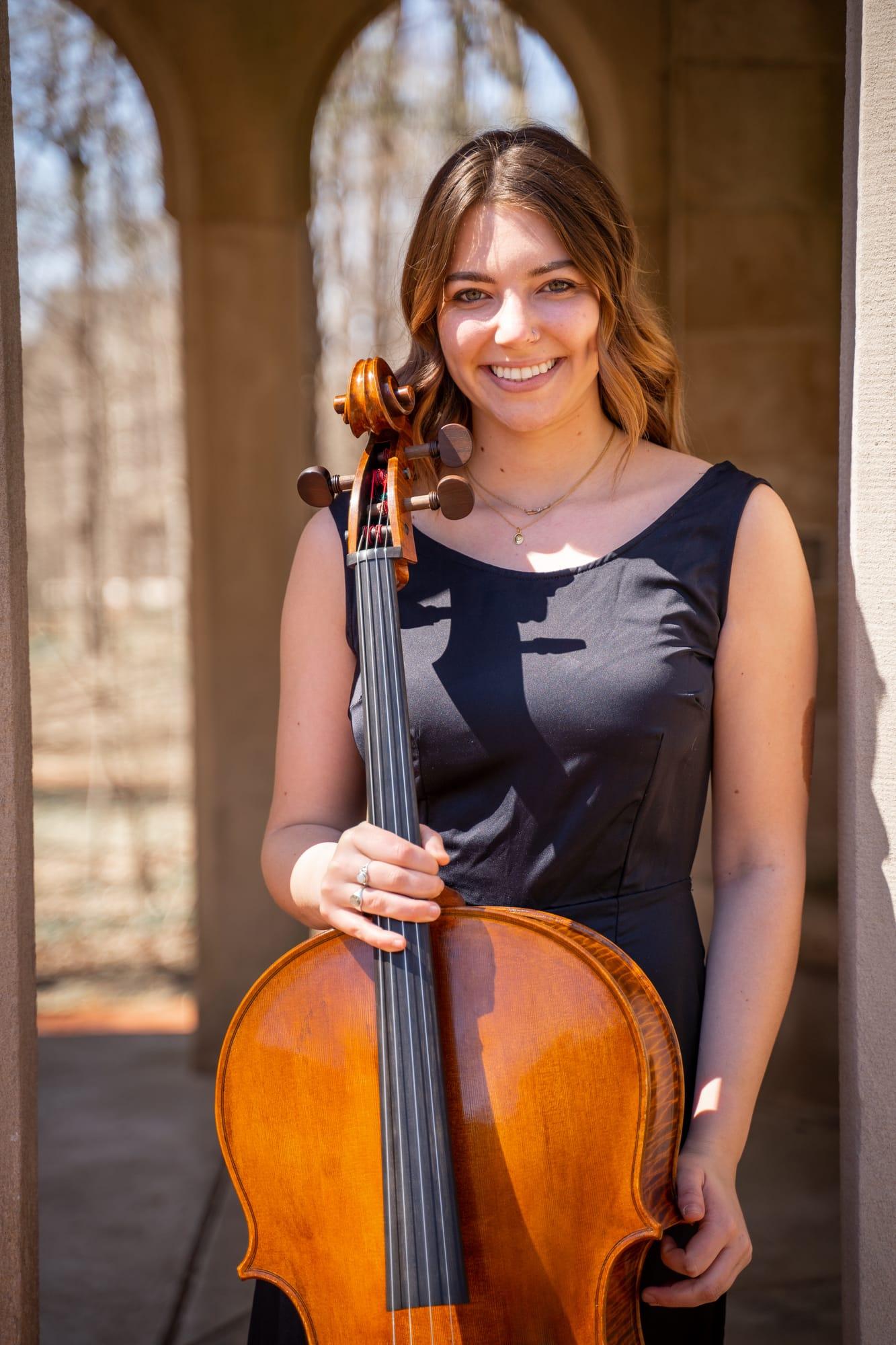 Olivia Hunt standing beneath a stone archway holding her cello